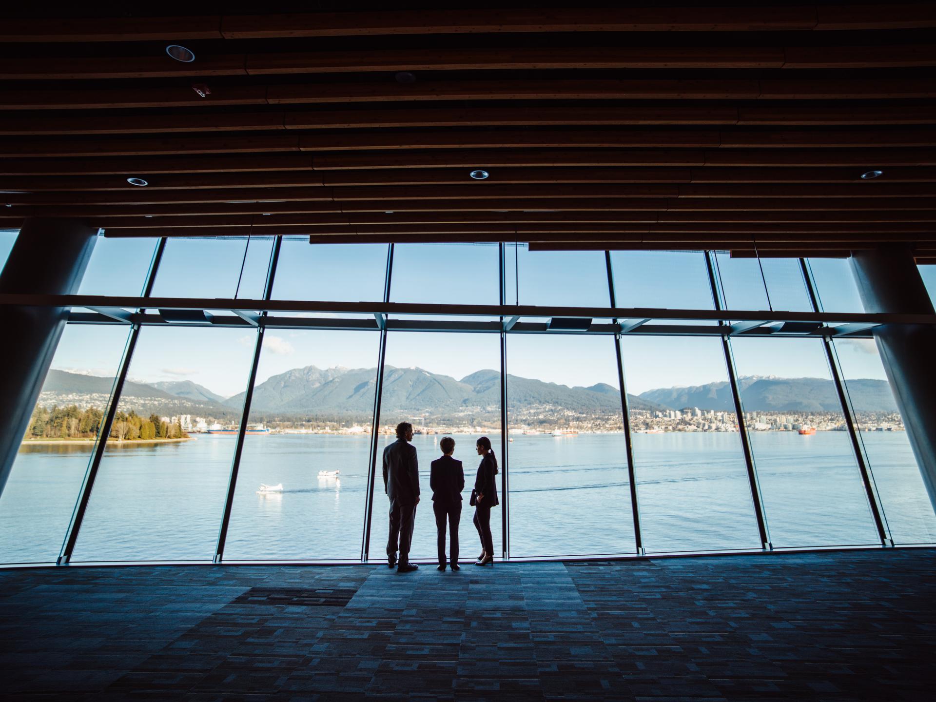 Trois personnes regardent les montagnes de Vancouver à travers une fenêtre.