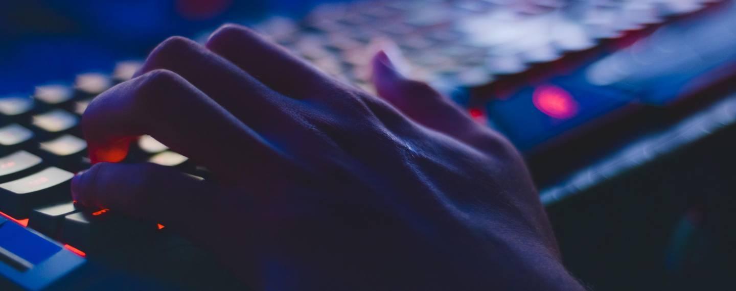 A hand typing on a light-up computer keyboard